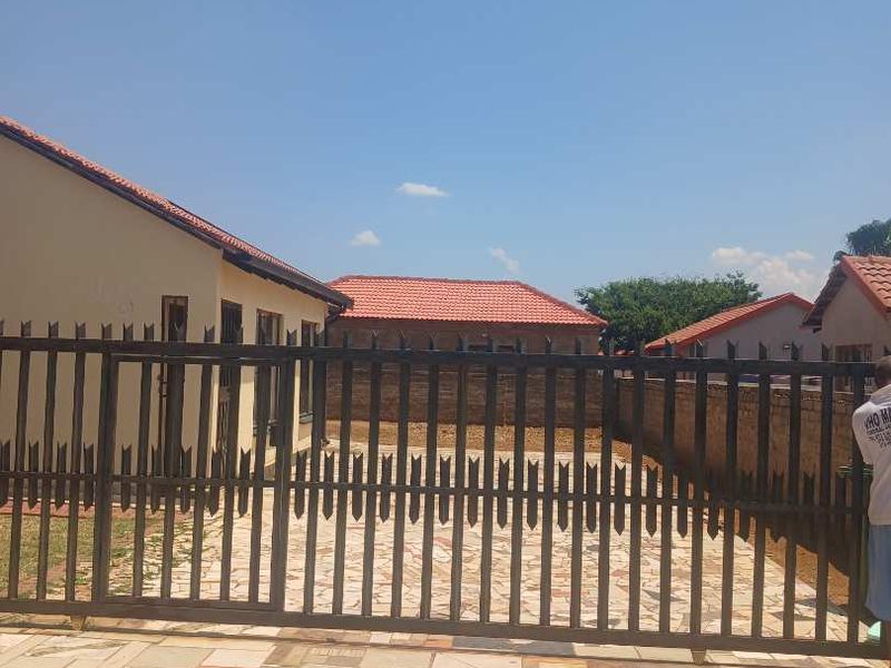 A view of the property entrance featuring a metal sliding gate, a tiled driveway, and surrounding brick boundary walls with tiled roof structures.