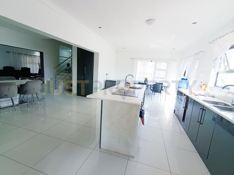 Spacious open-plan kitchen and living area featuring a central island, modern cabinetry, and tiled flooring, with an adjacent staircase.