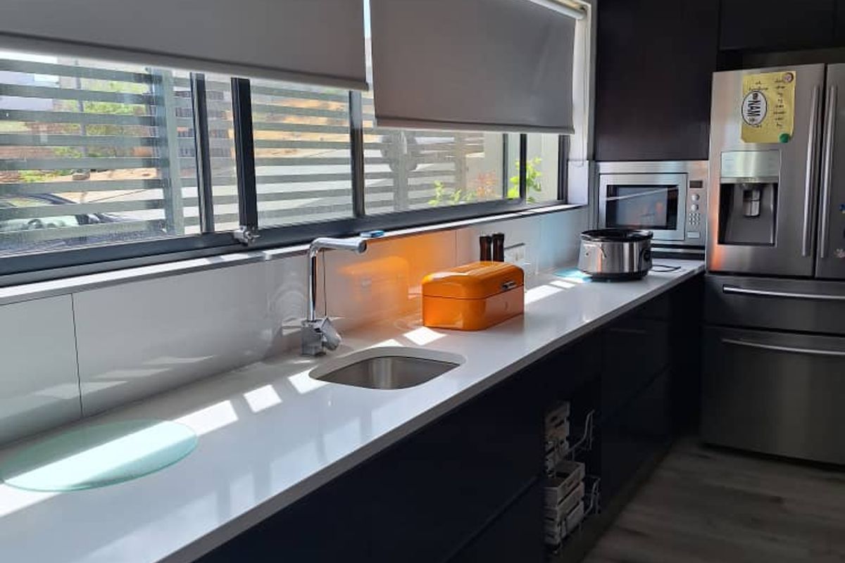 Modern kitchen featuring dark cabinetry, stone countertops, stainless steel sink, and integrated microwave, complemented by sleek roller blinds and wood-look flooring.
