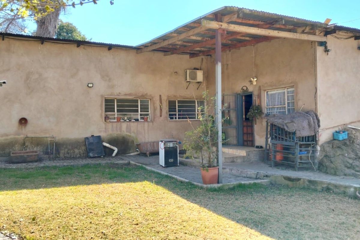 Rear exterior view of the property featuring a covered patio area, metal window frames, and a weathered facade requiring maintenance.