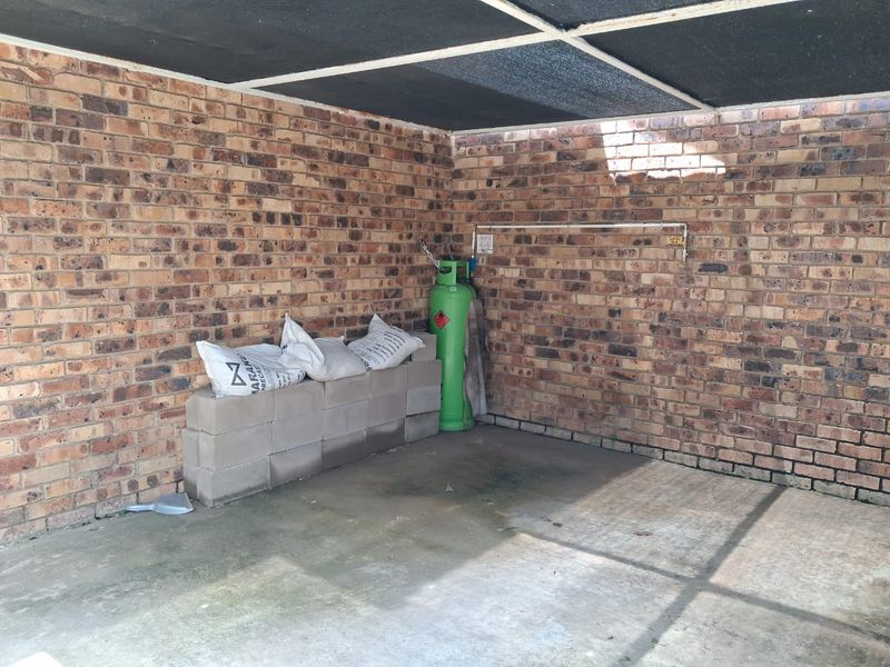 A functional garage space featuring exposed brick walls, a concrete floor, and a shade cloth roof structure, suitable for vehicle storage or utility use.