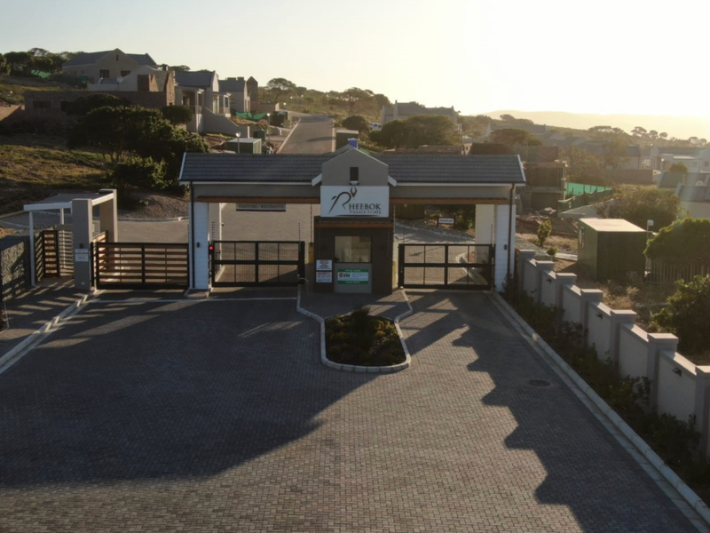 Aerial view of the secure entrance gate and paved access road for Rheebok Village Estate, featuring perimeter walls and security infrastructure.