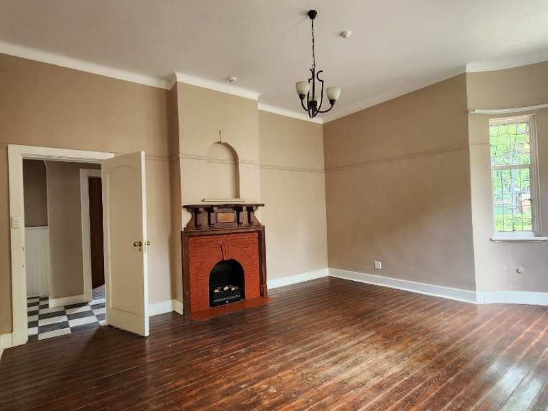Spacious living room featuring original timber flooring, a classic brick fireplace with mantelpiece, and charming leaded glass windows.