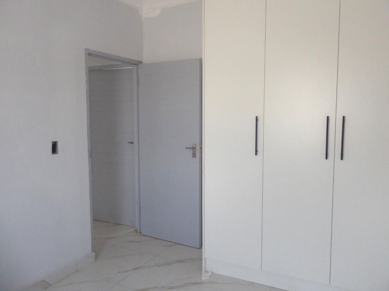 A clean, empty bedroom featuring modern white built-in cupboards, light-colored tiled flooring, and neutral wall finishes.