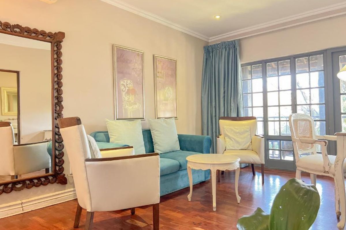 A well-maintained living room featuring polished wooden flooring, recessed ceiling lighting, a wall-mounted air conditioning unit, and French doors leading to an outdoor area.
