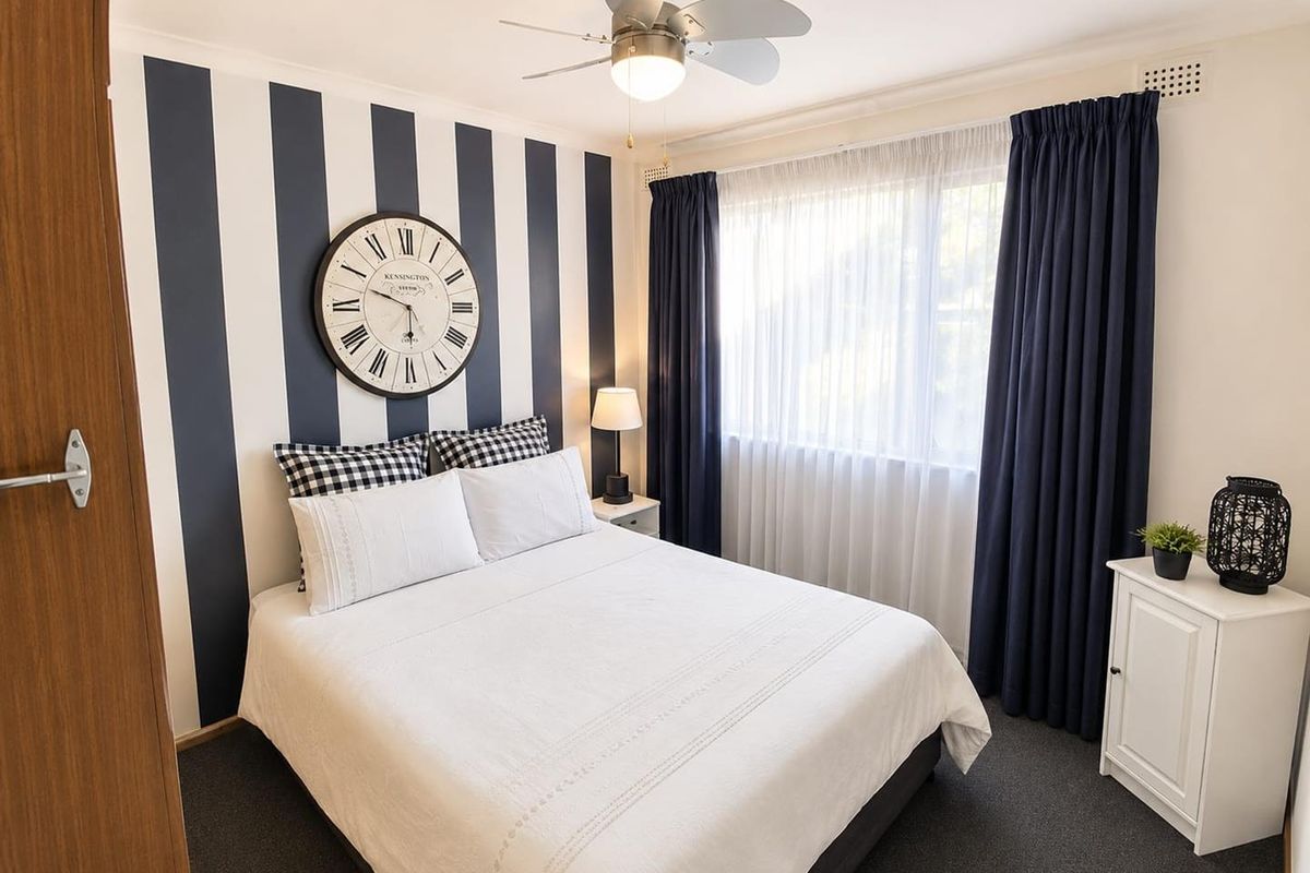 A well-maintained bedroom featuring a ceiling fan, carpeted flooring, and a large window with integrated curtain tracks.