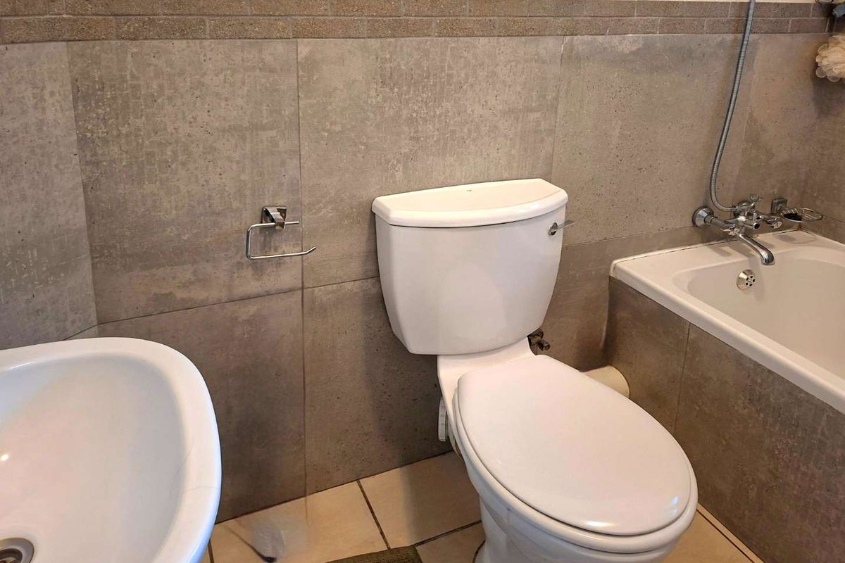 A functional bathroom featuring a standard toilet, bathtub with shower mixer, and basin, finished with neutral wall and floor tiling.
