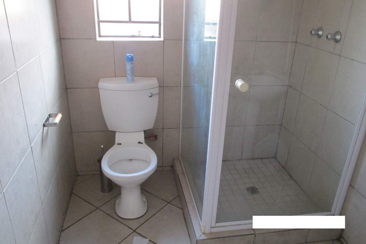 A functional bathroom featuring a standard toilet, a glass-enclosed shower, and neutral wall and floor tiling.