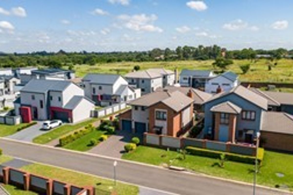 An aerial view of a modern residential estate featuring multiple detached houses with paved driveways, tiled roofs, and well-maintained garden spaces.