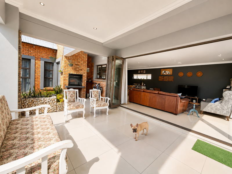 Spacious covered patio featuring tiled flooring, exposed brickwork, a built-in fireplace, and seamless bi-fold doors connecting to the indoor living area.