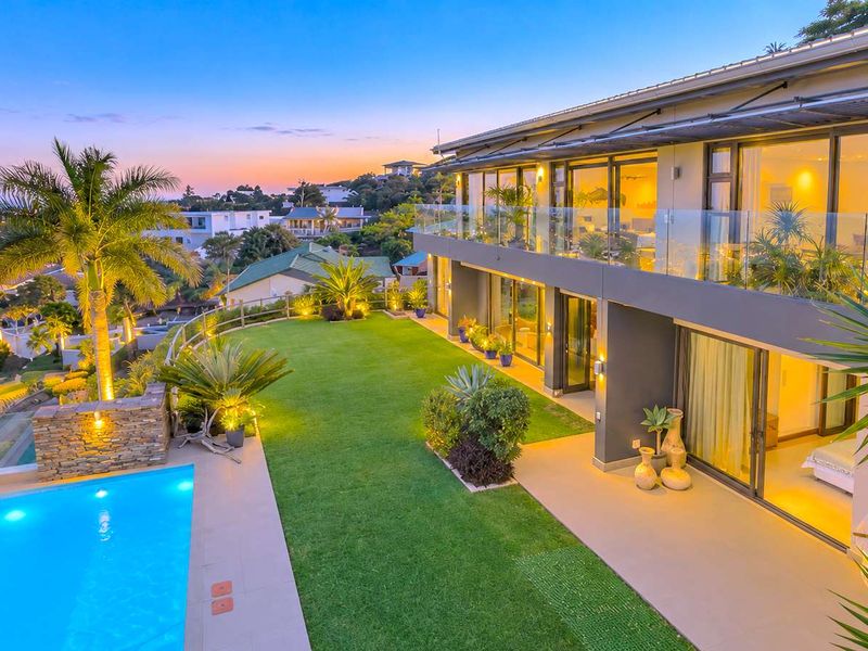 A beautifully maintained rear exterior featuring a swimming pool, landscaped lawn, and a modern multi-level home with extensive glass sliding doors and balcony.