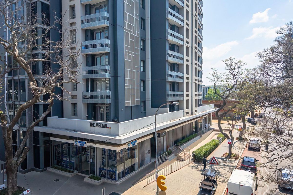 Aerial view of The Median apartment building, showcasing its modern facade, private balconies, and ground-level commercial retail space in an urban setting.