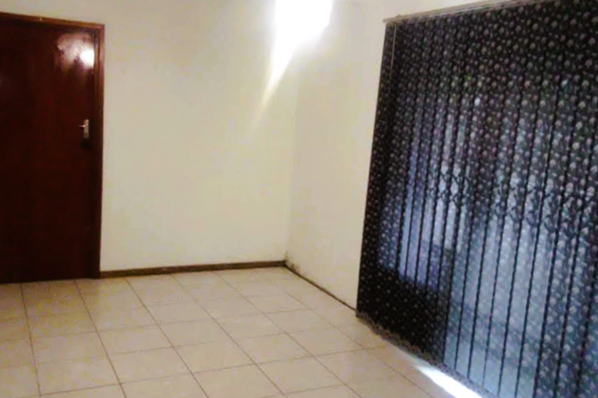 An empty room featuring tiled flooring, a dark wooden door, and large window covered by vertical blinds.