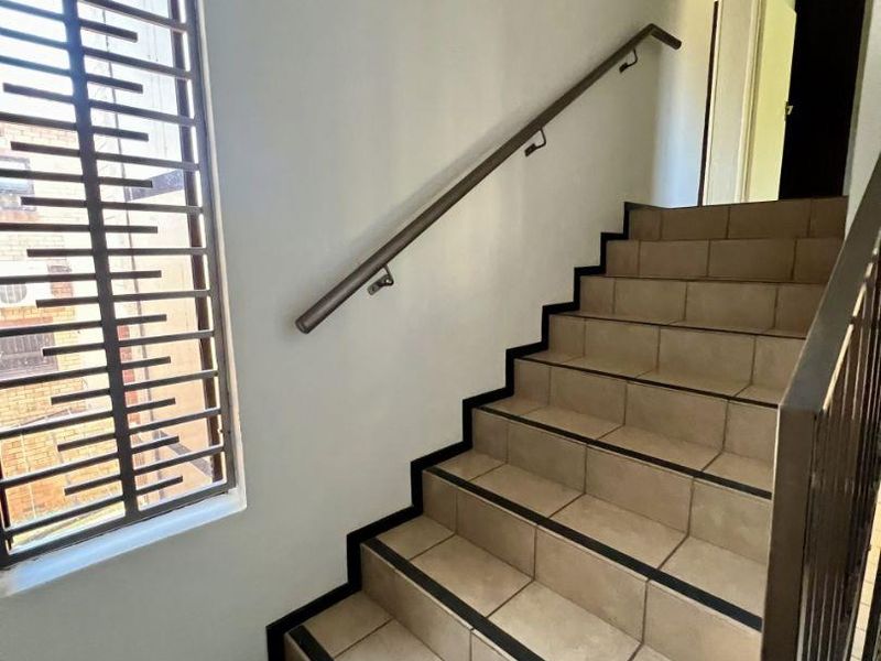 A clean, functional staircase featuring tiled steps, a secure metal handrail, and a large window with security bars for natural light.