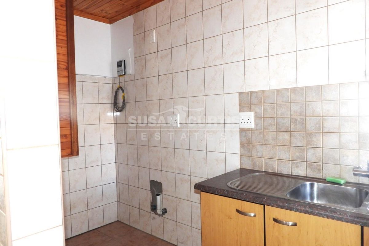 A compact kitchen area featuring timber ceiling, tiled walls, and basic cabinetry with a stainless steel sink, currently in need of cosmetic updates.