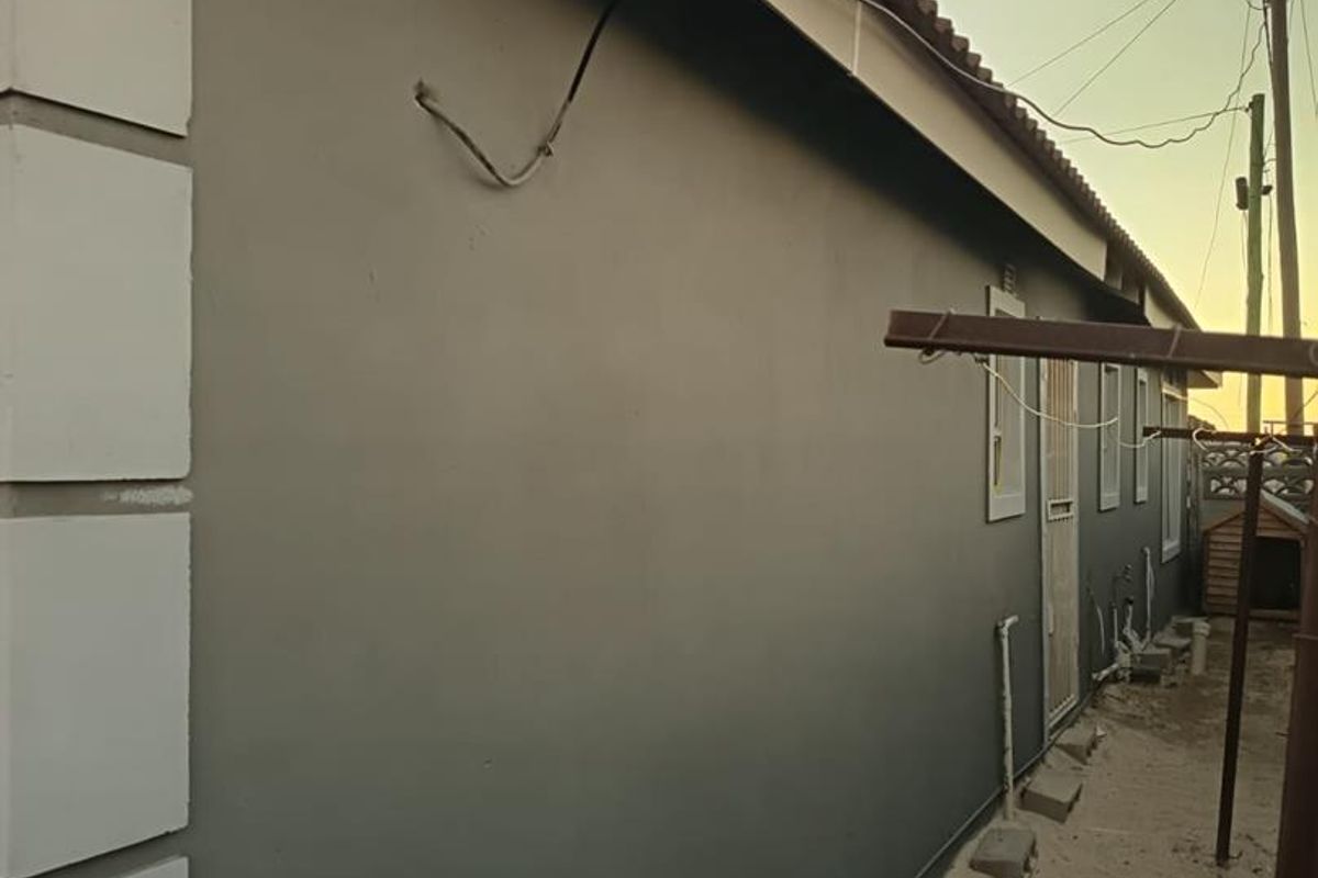 A side view of the property exterior showing a rendered wall, tiled roof, and exposed utility wiring and plumbing pipes.