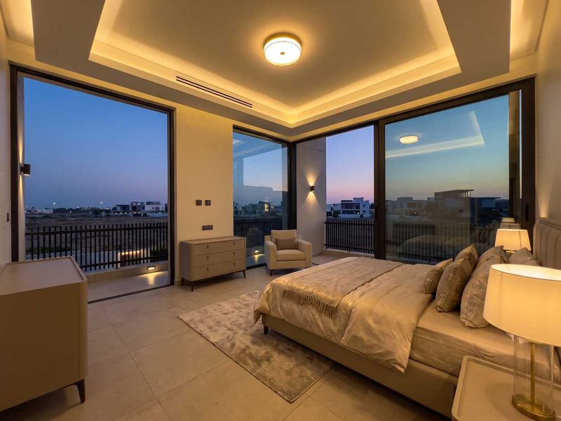 Modern bedroom featuring high ceilings with cove lighting, expansive floor-to-ceiling windows, and direct access to a private balcony with scenic views.