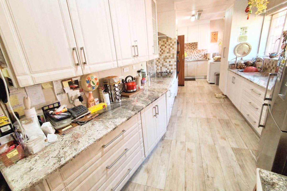 A functional kitchen featuring granite countertops, ample built-in cabinetry, a tiled backsplash, and wood-look tile flooring throughout the space.