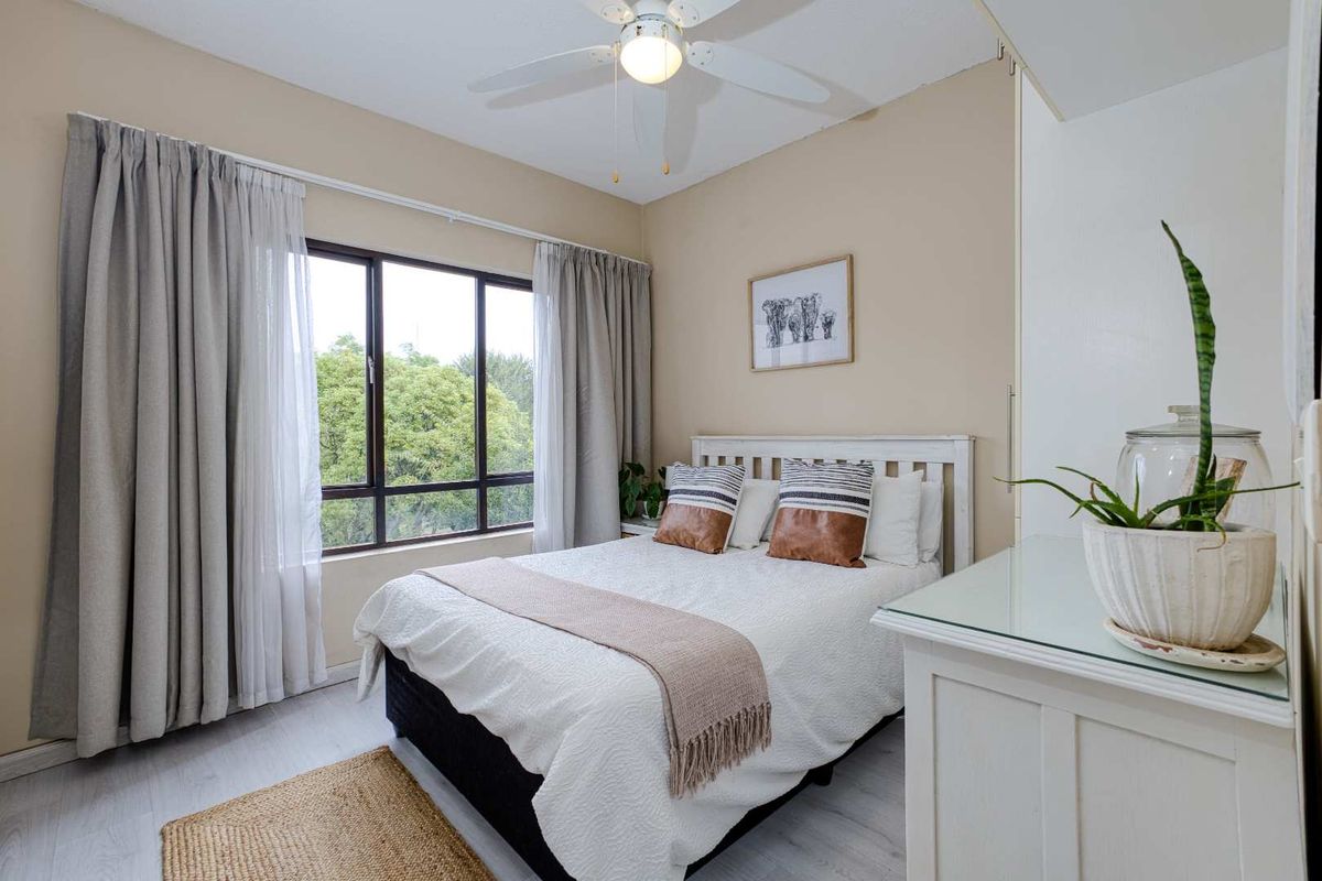 A bright and well-maintained bedroom featuring a ceiling fan, built-in wardrobe, and large window with natural light.