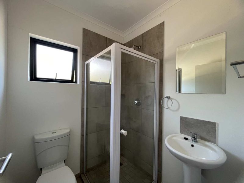 A functional bathroom featuring a shower enclosure, pedestal basin, and toilet with neutral wall tiling.