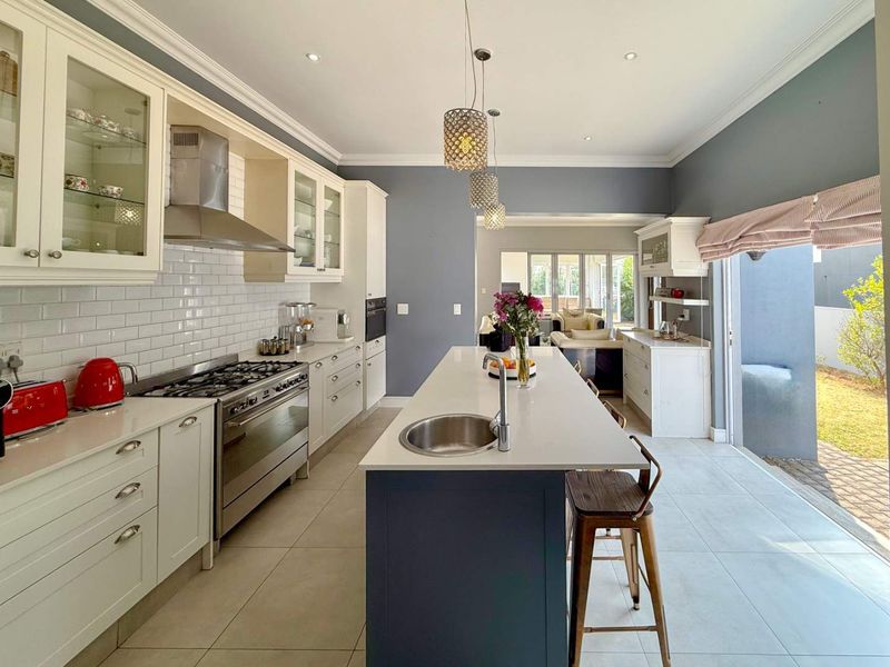 Modern kitchen featuring a large central island, gas stove, subway tile backsplash, and ample built-in cabinetry, flowing into an adjacent living area.