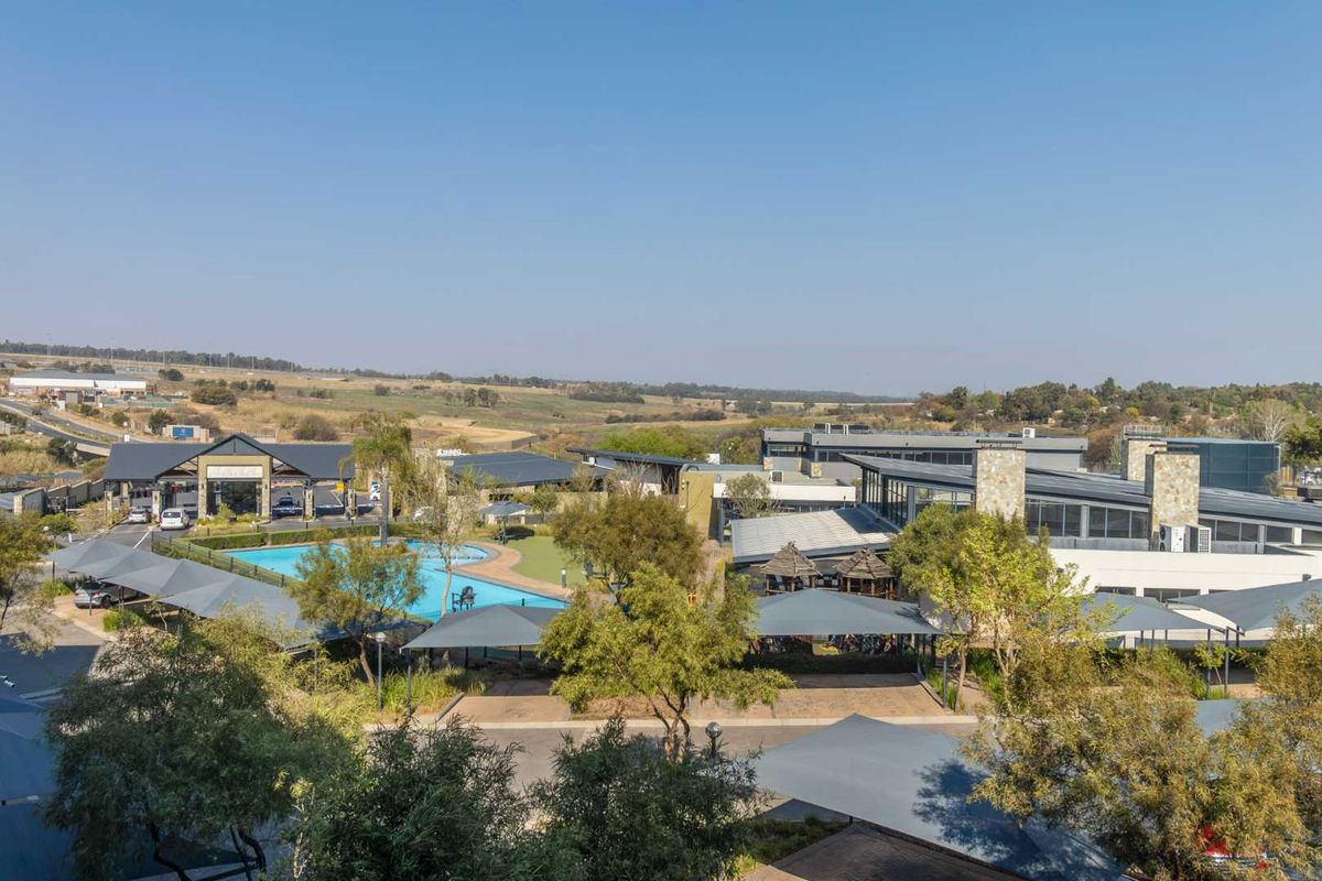 An aerial view of the apartment complex grounds, featuring a swimming pool, shaded parking areas, landscaped gardens, and the estate entrance.