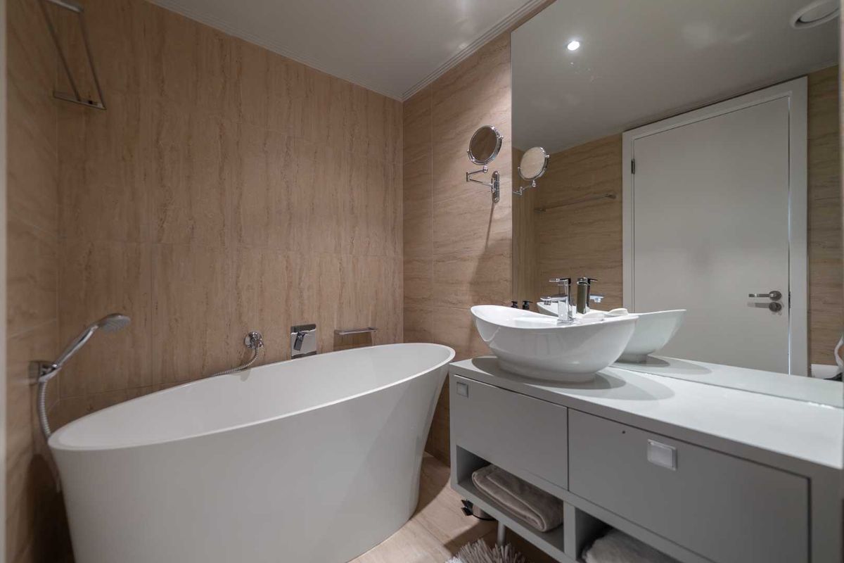 Modern bathroom featuring a sleek freestanding bathtub, contemporary vessel sink vanity, and floor-to-ceiling tiled walls with a large integrated mirror.