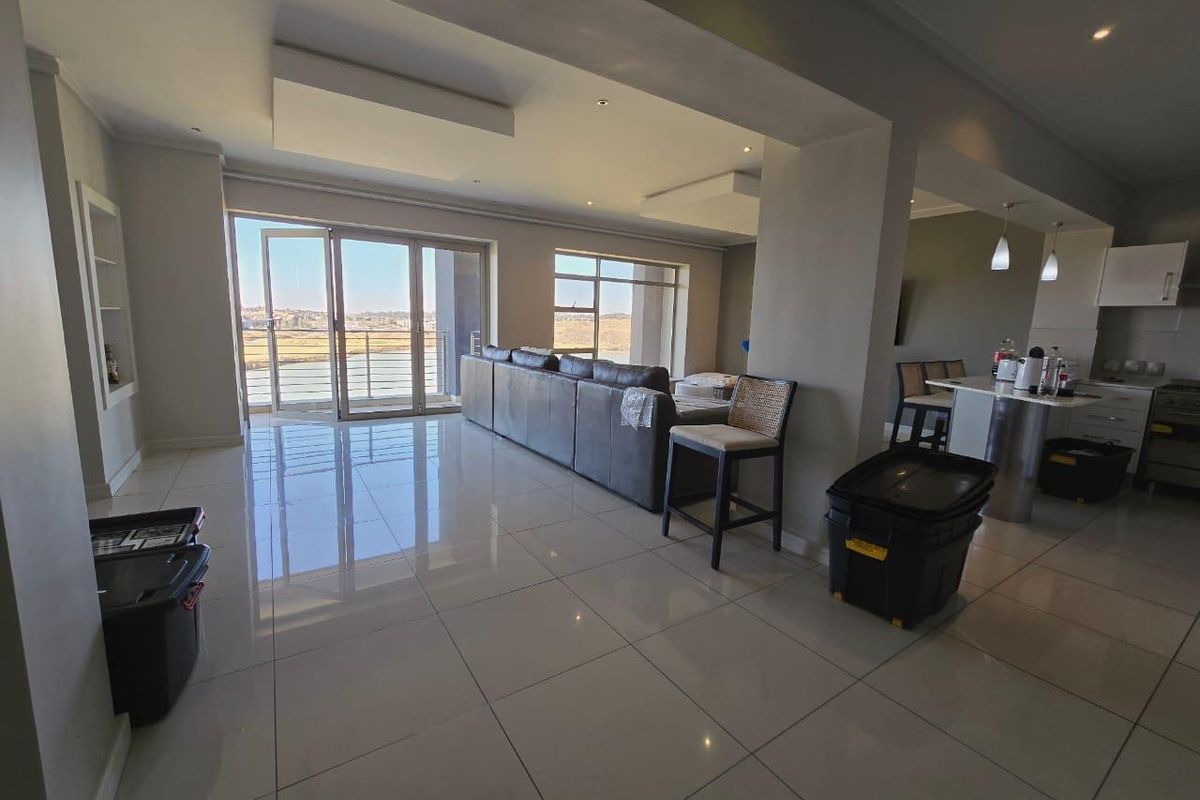 Spacious open-plan living and kitchen area featuring large format floor tiles, modern recessed lighting, and direct access to a balcony with scenic views.