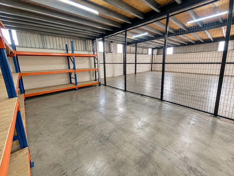 A spacious industrial utility area featuring concrete floors, exposed steel ceiling beams, wire mesh partitioning, and built-in industrial shelving units.