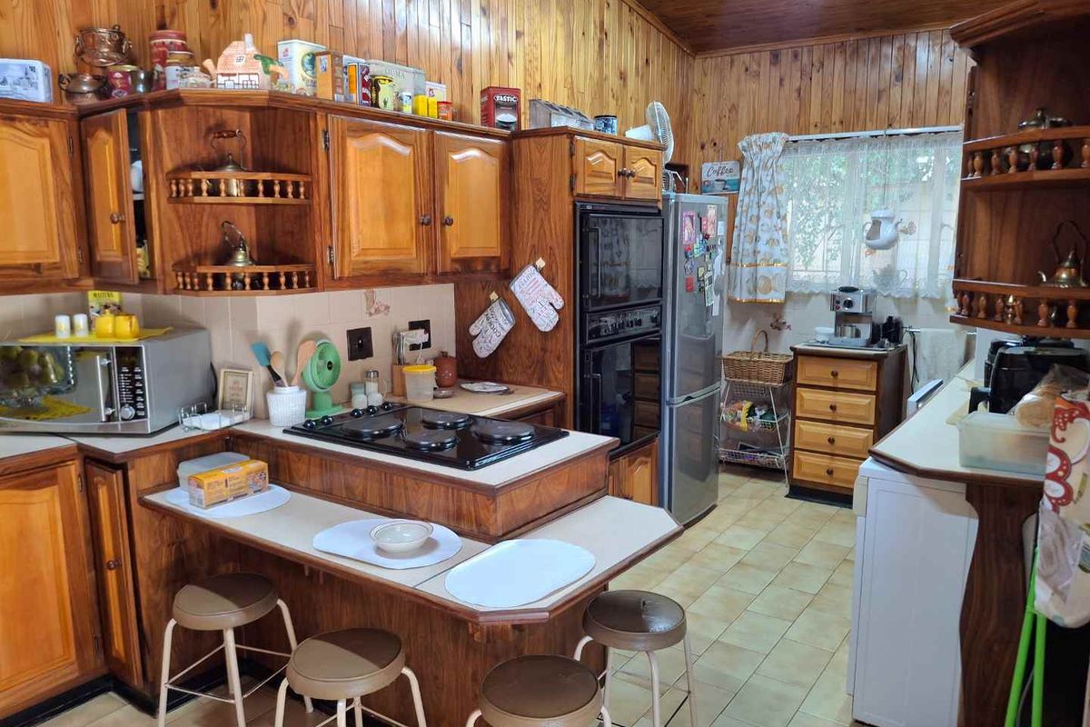 A traditional kitchen featuring extensive wooden cabinetry, a built-in double oven, electric hob, and tiled flooring with warm wood-paneled walls.