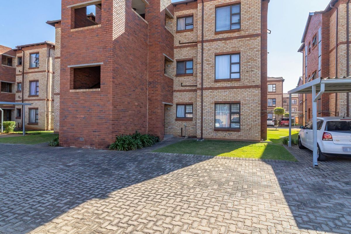Exterior view of a multi-story face brick townhouse complex featuring paved driveway areas and covered parking carports.