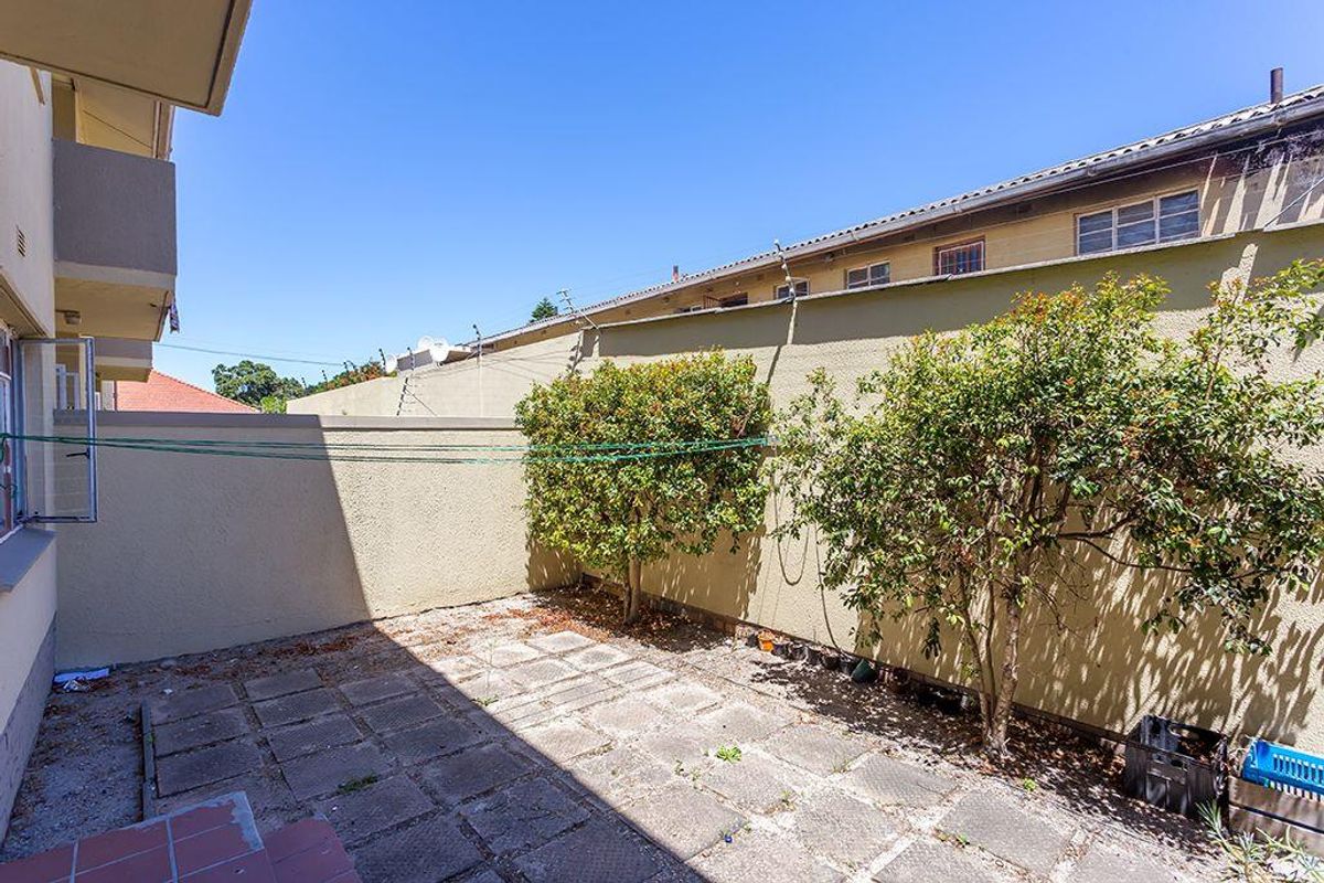 A private rear courtyard featuring paved flooring, perimeter walling with electric fencing, and established shrubs, offering potential for a refreshed outdoor living space.