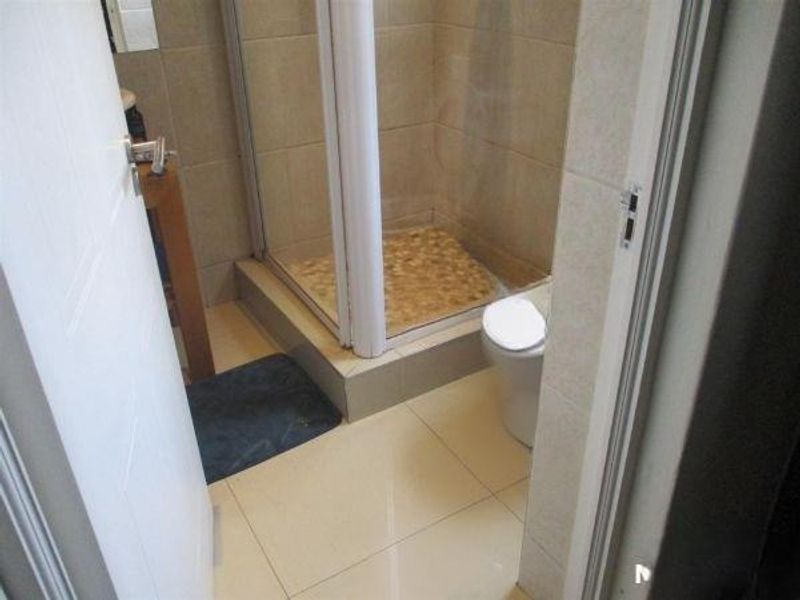 A compact bathroom featuring a shower enclosure with a pebble-tiled floor, a toilet, and neutral ceramic wall and floor tiling.