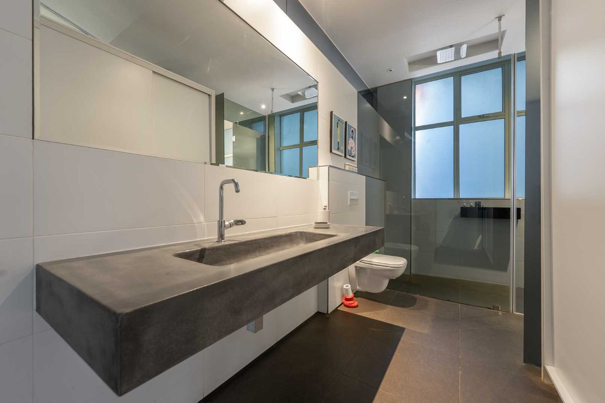 Modern bathroom featuring a sleek concrete vanity with integrated basin, wall-hung toilet, and a spacious glass-enclosed shower area with contemporary finishes.