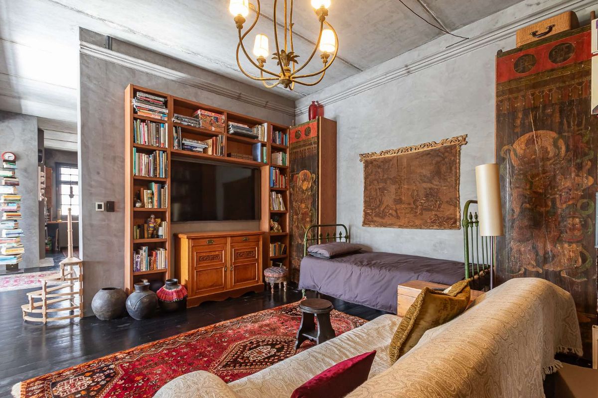 A characterful bedroom featuring exposed concrete ceilings, dark hardwood flooring, and a large built-in wooden shelving unit with integrated television space.