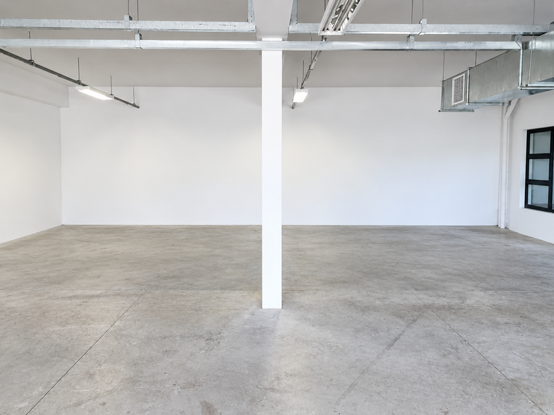 Spacious open-plan industrial unit featuring polished concrete floors, exposed ceiling ducting, and ample natural light through black-framed windows.