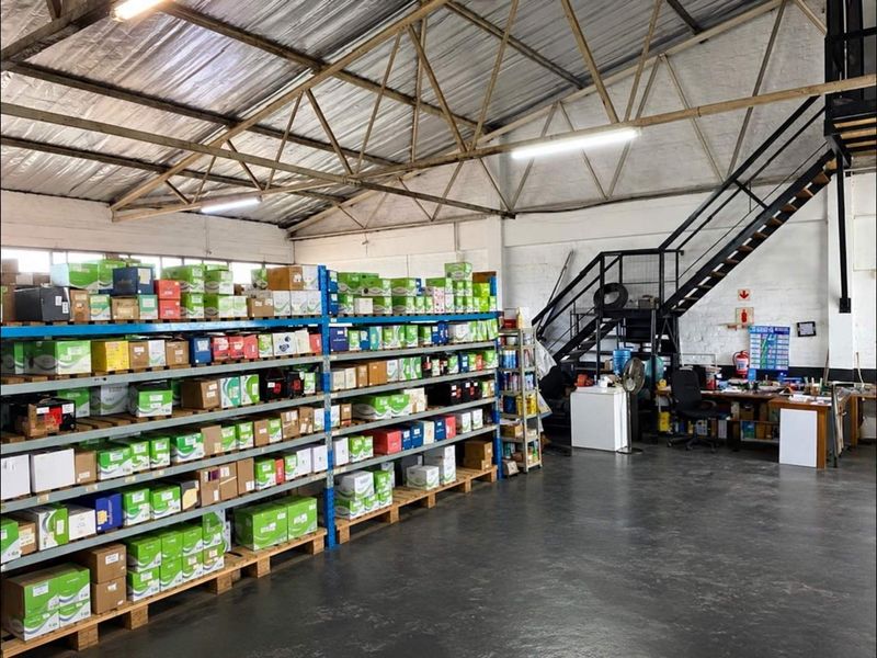 Industrial warehouse space featuring high ceilings with exposed steel trusses, concrete flooring, and a mezzanine access staircase.