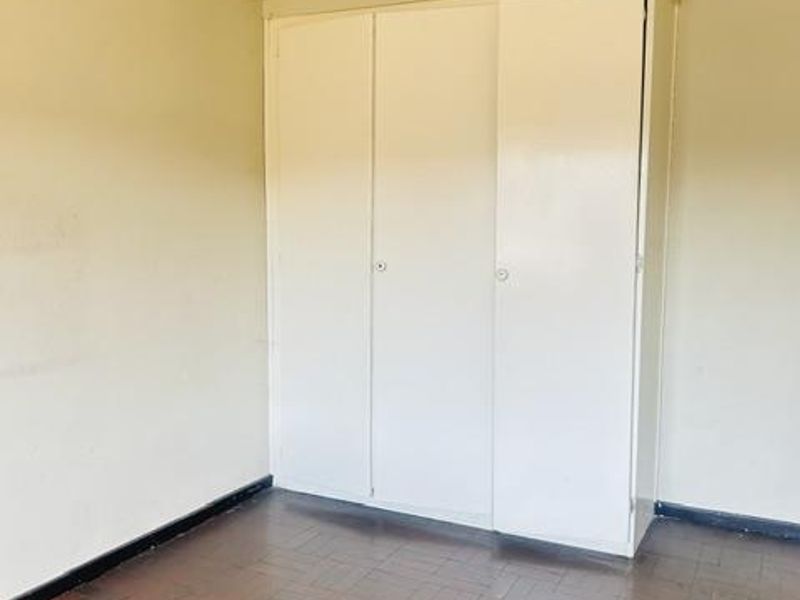 An empty bedroom featuring parquet flooring, a built-in wardrobe, and crown molding, offering a blank canvas for renovation or staging.