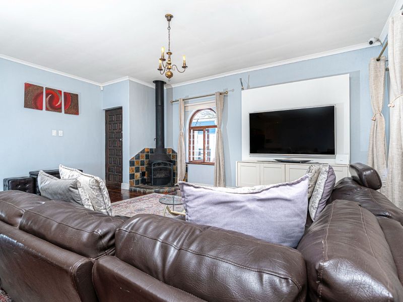 A comfortable living room featuring a freestanding fireplace with tiled hearth, built-in media cabinetry, and an arched window, finished with hardwood flooring.