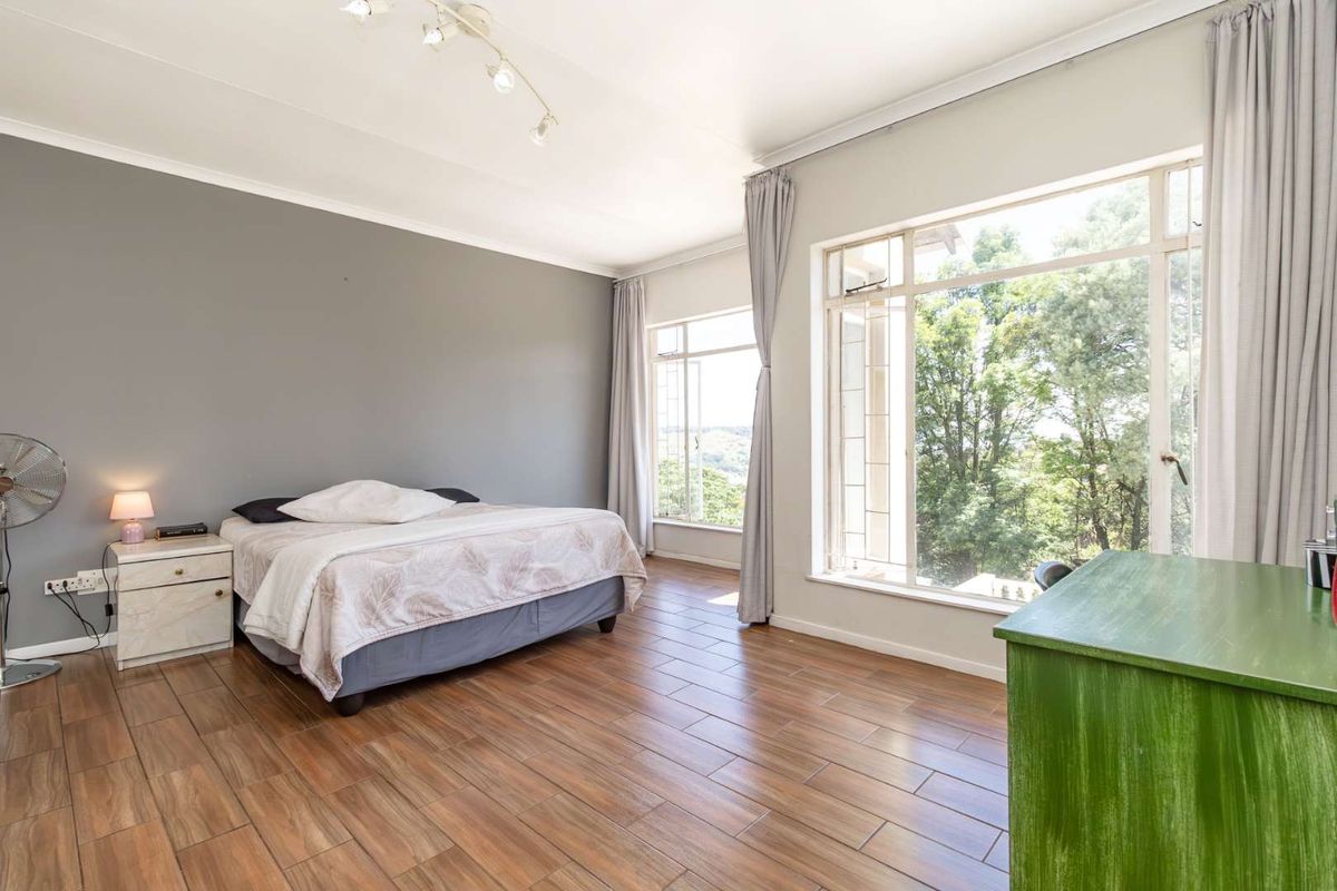 Spacious bedroom featuring wood-look tile flooring, large windows with natural light, and neutral wall finishes.