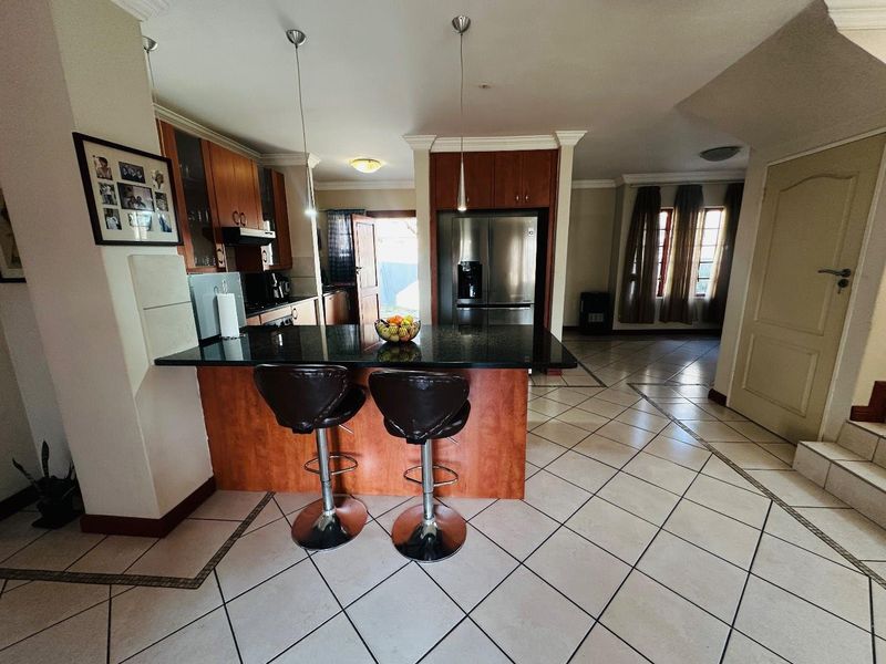 Open plan kitchen featuring a central island with granite countertops, wooden cabinetry, and tiled flooring, seamlessly connecting to the living area.