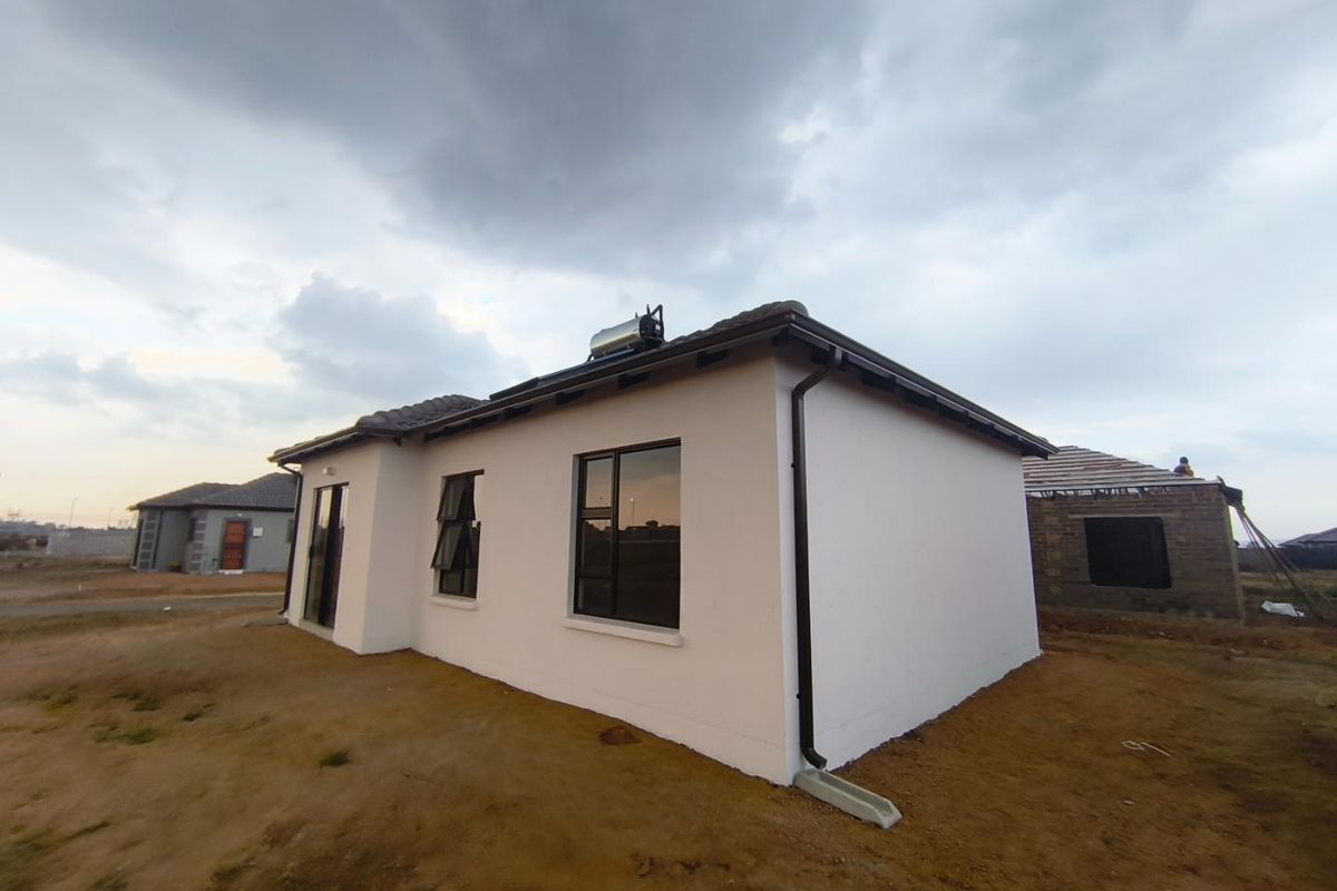 A modern single-story residential home featuring a white rendered facade, dark window frames, and a roof-mounted solar geyser system.