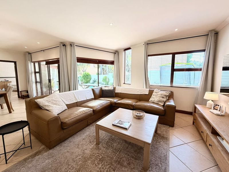 A bright and spacious living room featuring large windows, sliding glass doors, tiled flooring, and recessed downlighting, creating an inviting and airy atmosphere.