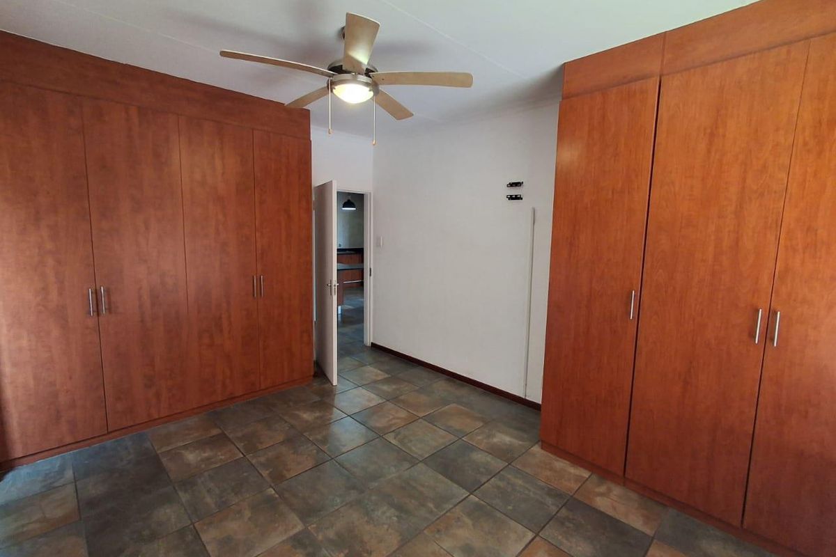 A spacious bedroom featuring extensive built-in wooden cupboards, a ceiling fan, and durable tiled flooring, offering a clean and functional living space.