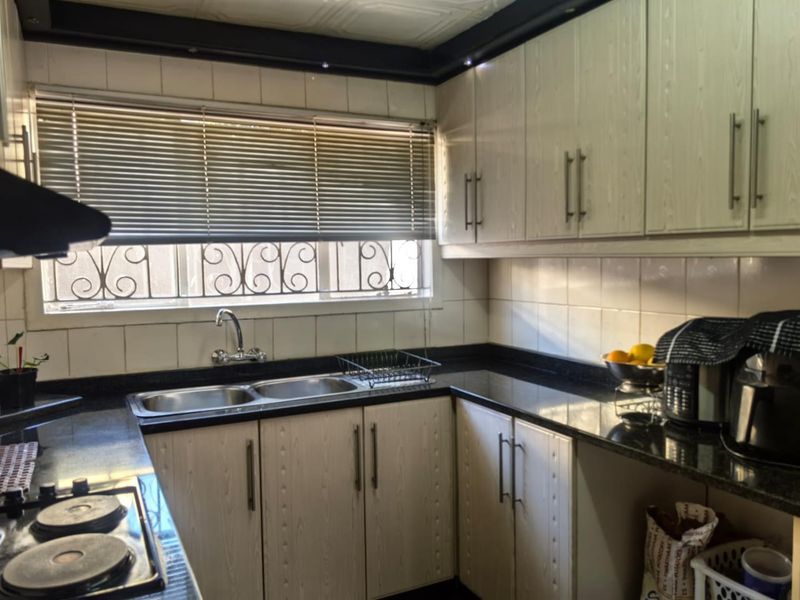 A functional kitchen featuring laminate cabinetry, granite countertops, a double basin sink, and a built-in hob with a tiled backsplash.