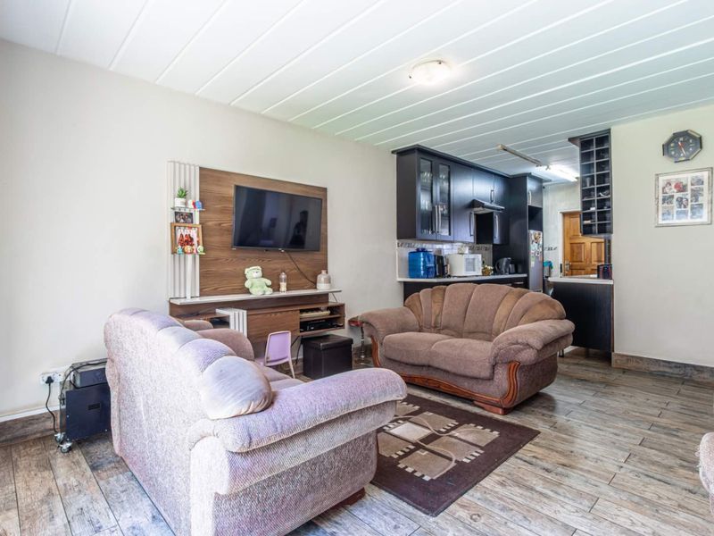 Open plan living area featuring wood-look tile flooring, tongue and groove ceiling, and a compact kitchen with dark cabinetry and built-in wine storage.