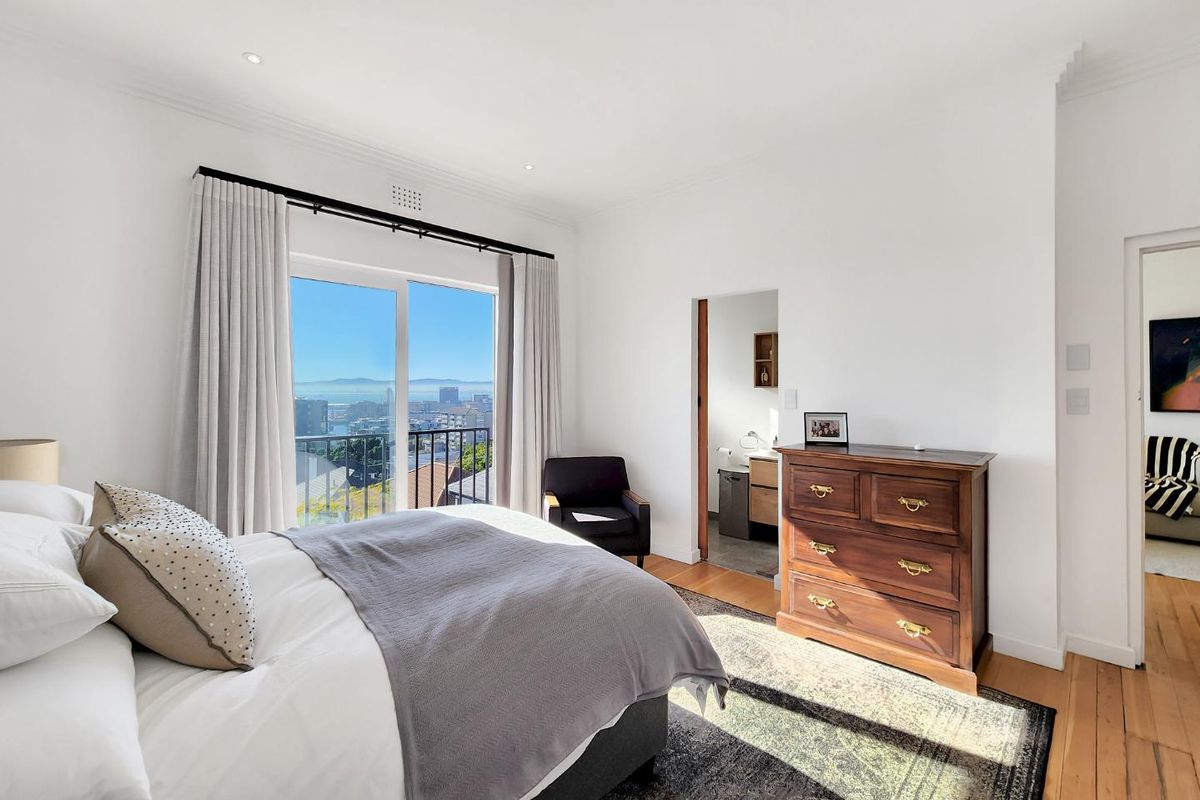 Bright bedroom featuring hardwood floors, recessed lighting, and a sliding glass door leading to a balcony with expansive city and ocean views.