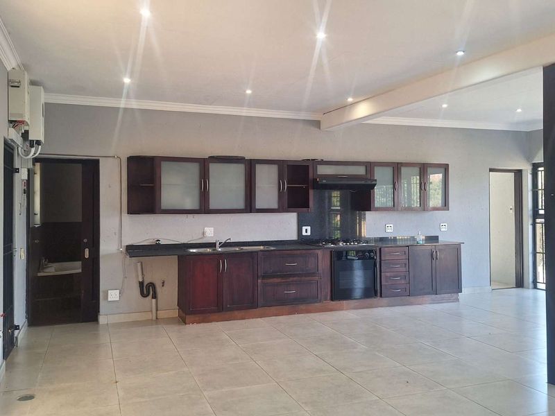 Spacious open-plan kitchen featuring dark wood cabinetry, built-in oven and hob, and tiled flooring, offering a functional layout for modern living.