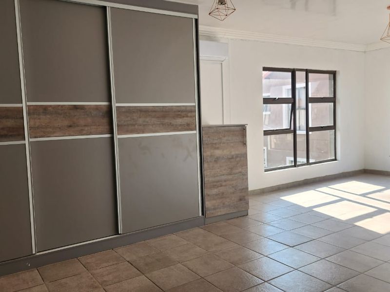 Spacious bedroom featuring modern built-in sliding door wardrobes, tiled flooring, air conditioning, and large windows providing ample natural light.