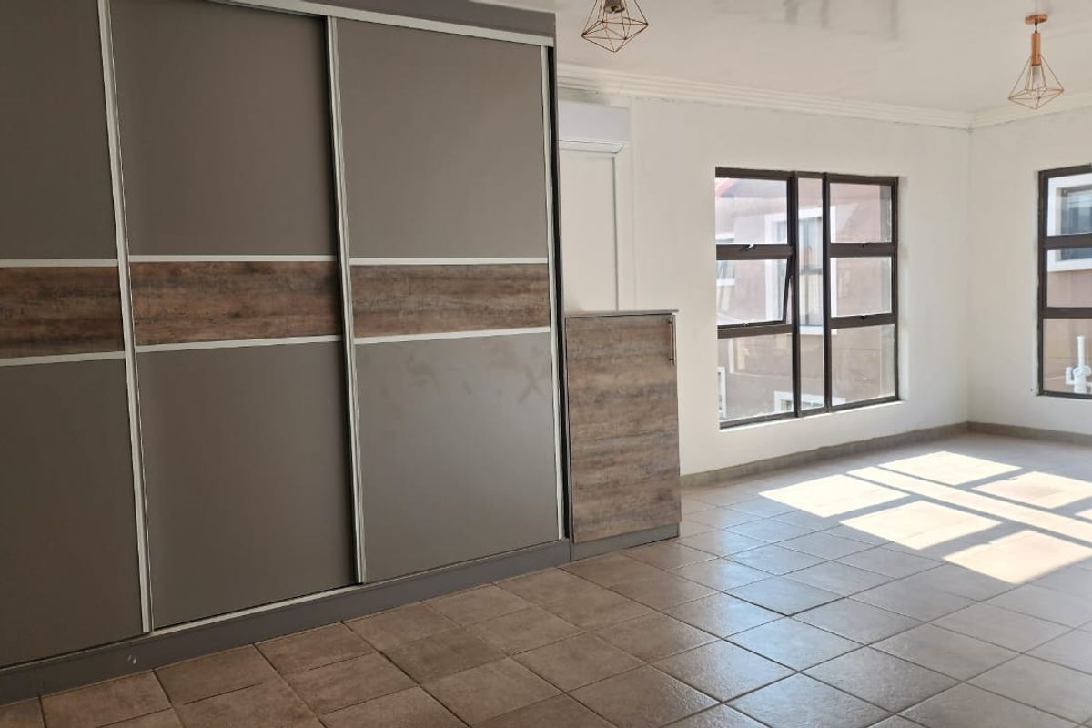 Spacious bedroom featuring modern built-in sliding door wardrobes, tiled flooring, air conditioning, and large windows providing ample natural light.